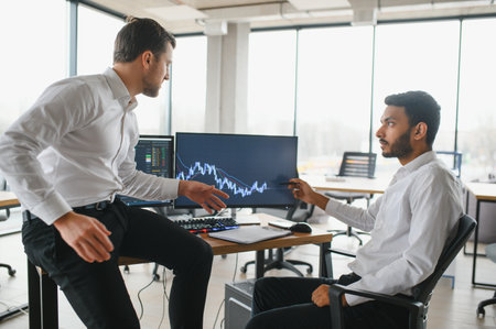 Two successful trader sitting in office and looking at screen, checking cryptocurrency information data on finance market graph, pointing on monitor.の写真素材