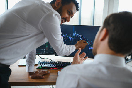 Two successful trader sitting in office and looking at screen, checking cryptocurrency information data on finance market graph, pointing on monitor.の写真素材