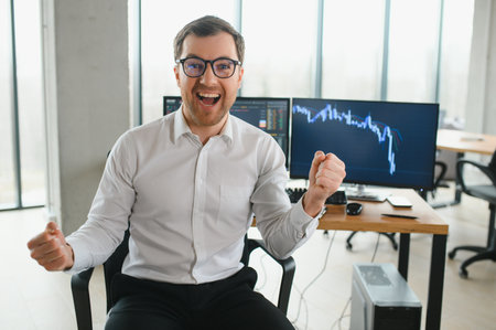 Young bearded man trader at office sitting at table looking camera smiling cheerful.の写真素材