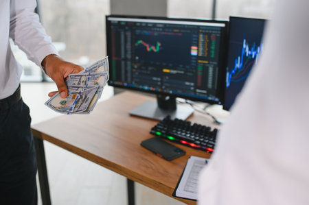 Two men traders sitting at desk at office together looking at data analysis discussing brainstorming...