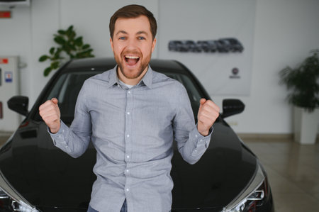 Emotional handsome guy raising hand up and smiling at camera. Rich man buying auto at luxury...