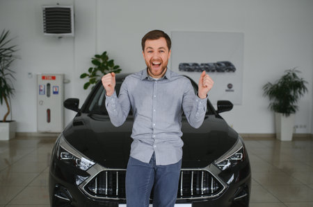 Emotional handsome guy raising hand up and smiling at camera. Rich man buying auto at luxury dealership salon.の写真素材