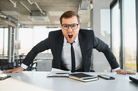 Angry businessman sitting at his desk and screaming at his employeesの写真素材