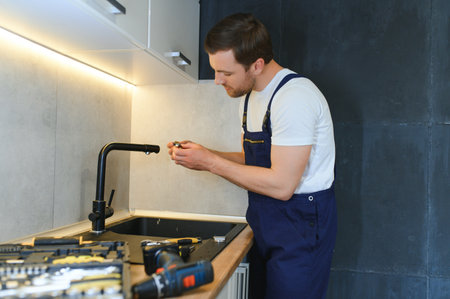 Happy Young Male Plumber Fixing Faucet In Kitchen.の写真素材