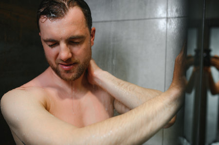 Relaxing after a stressful day. Waist up portrait of naked muscular gentleman taking shower at homeの写真素材