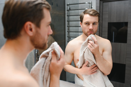 Young man looking in mirror after shaving at home.の写真素材