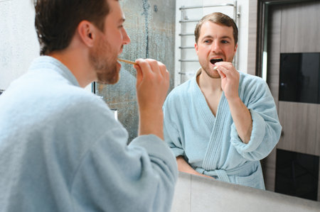 brushing teeth in the morning. Rear view of handsome young beard man brushing his teeth and smiling while standing against a mirrorの写真素材