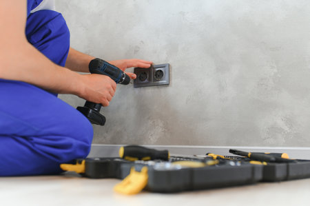 Smiling professional electrician in uniform replacing a socket in apartment after renovation work.の写真素材