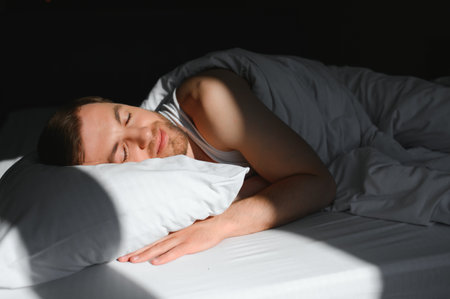 Handsome man sleeping under soft blanket in bed at home, above view.