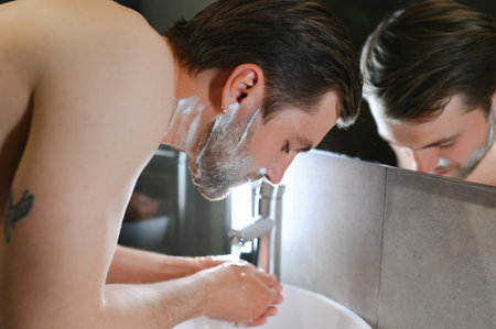 Bright caucasian man spraying water on his face after shaving in the bathroom at home.の写真素材