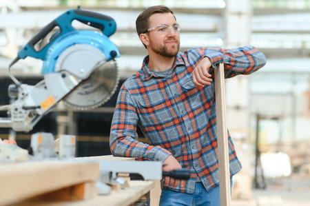 A carpenter works on woodworking the machine tool. Man collects furniture boxes. Saws furniture details with a circular saw. Process of sawing parts in parts. Against the background of the workshopの写真素材