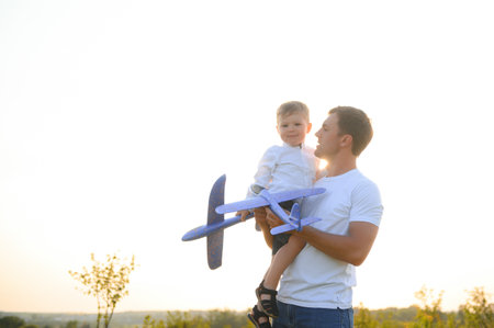 happy father child moment. Father piggybacking his boy at sunset while he's playing with toy planeの写真素材