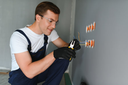 Electrician with screwdriver repairing power socket in room.