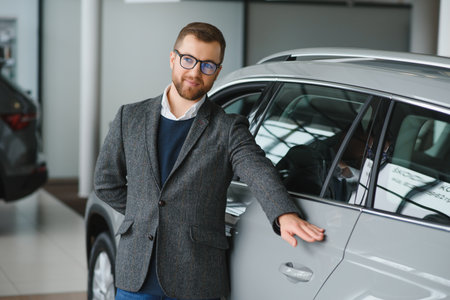 visiting car dealership. Handsome bearded man is stroking his new car and smiling.の写真素材