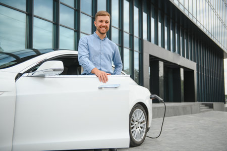 portrait of young handsome man in casual wear, standing at the charging station. Eco electric car...