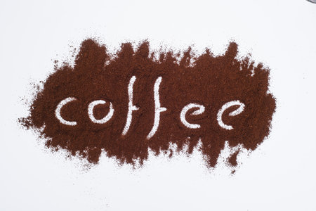 Coffee word written on ground coffee layer, white background.