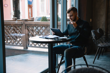 Handsome businessman using a digital tablet and drinking coffee while sitting in cafe in the city centerの写真素材