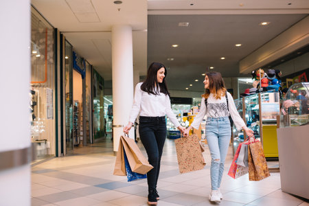 Beautiful young mom and teenage daughter are holding shopping bags and smiling while doing shopping...