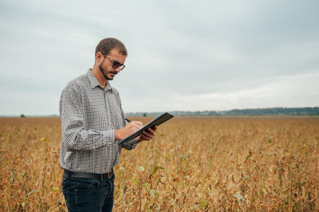 handsome agronomist holds tablet touch pad computer in the soy field and examining crops before harvesting. Agribusiness concept. engineer standing in a soy agricultural field with a tablet.の写真素材