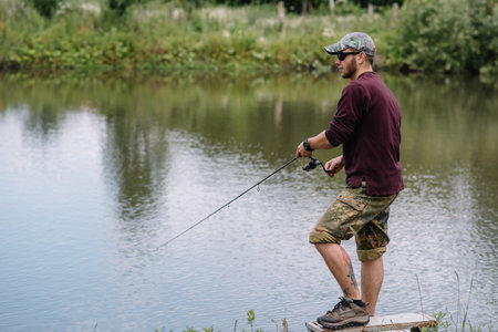 Fishing in river.A fisherman with a fishing rod on the river bank. Man fisherman catches a fish pike.Fishing, spinning reel, fish, Breg rivers. - The concept of a rural getaway. Article about fishing.の写真素材