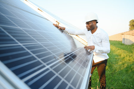An African-American engineer in a white shirt and hard hat is working on a field of solar panels. solar renewable energy conceptの写真素材