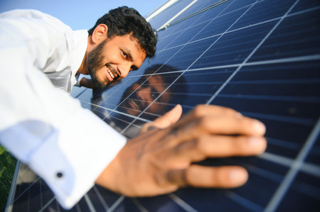 Male arab engineer standing on field with rows of solar panels