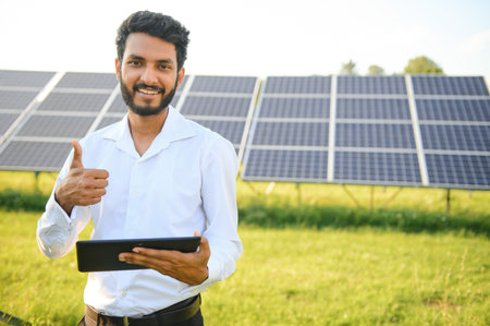 male engineer checks a photovoltaic (solar) plant and uses a recording tablet. Indian Man in uniform...