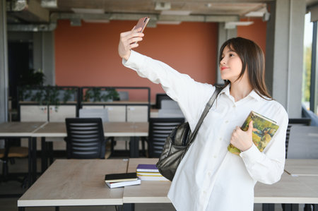 Portrait of a happy cheerful smiling young student schoolgirl lady with long hair standing in empty classroom looking camera take a selfie.の写真素材