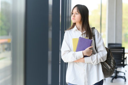 Schoolgirl standing with books and backpack at schoolの写真素材