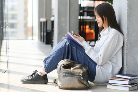 educational concept. A modern girl student sits on the floor and read joyfully a book. Modern...