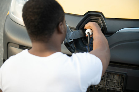african man holding charge cable in on hand standing near electric car.