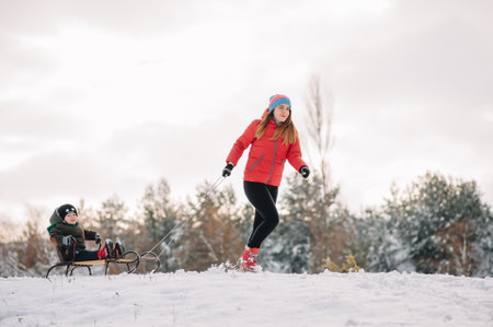 A father is carrying a child on a sled. Father walks with her son over the snow-covered forest. Cheerful winter holidays. winter fun. Baby on the sleigh.の写真素材