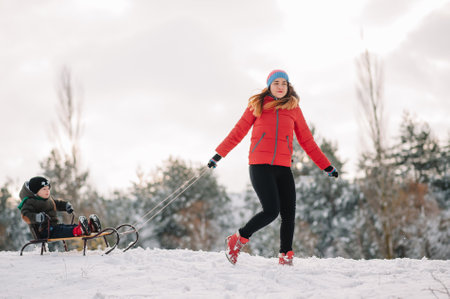 A father is carrying a child on a sled. Father walks with her son over the snow-covered forest. Cheerful winter holidays. winter fun. Baby on the sleigh.の写真素材
