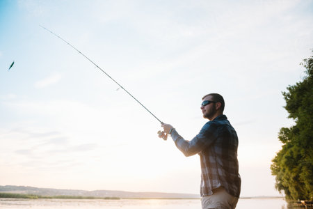 Fisher man fishing with spinning rod on a river bank at misty foggy sunrise. fisher with spinning. spinning conceptの写真素材