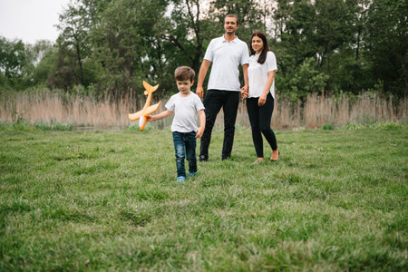 Father, mother and son playing with toy airplane in the park. friendly family. People having fun outdoors. Picture made on the background of the park and blue sky. concept of a happy family.の写真素材