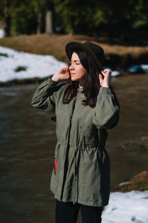 woman in a hat and green jacket is resting on the nature in the mountains near the mountain river. Relax time on holiday concept travelの写真素材