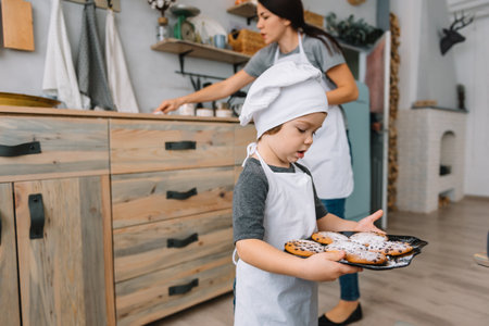Young happy mom and her baby cook cookies at home in the kitchen. Christmas Homemade Gingerbread. cute boy with mother in white uniform and hat cooked chocolate cookies.の写真素材