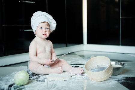 Little boy sitting on carpet in kitchen playing with cooking pots. Cute boy cooking in the kitchen at homeの写真素材