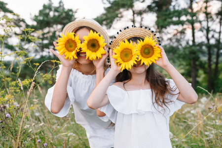 Cheerful mother and her little daughter having fun together in the summer background. Happy family in nature background. Cute girls with colorful flowers.の写真素材