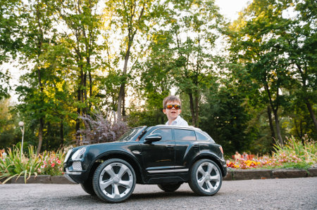 Cute boy riding a black electric car in the park. Funny boy rides on a toy electric car. little...