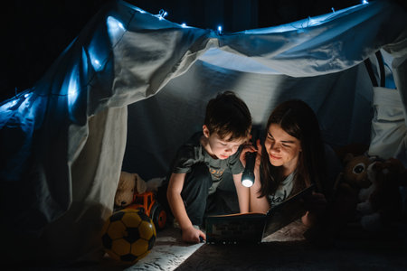 happy family mother and child son reading a book with a flashlight in a tent at home. family conceptの写真素材