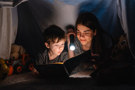 happy family mother and child son reading a book with a flashlight in a tent at home. family concept