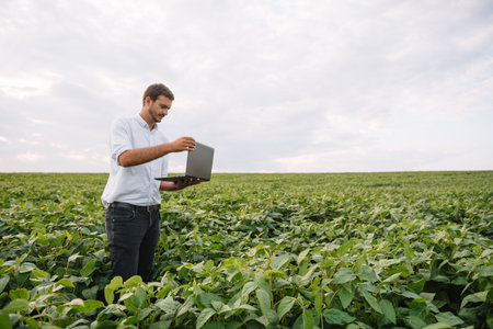 Agronomist inspecting soya bean crops growing in the farm field. agriculture production concept. young agronomist examines soybean crop on field in summer. Farmer on soybean fieldの写真素材