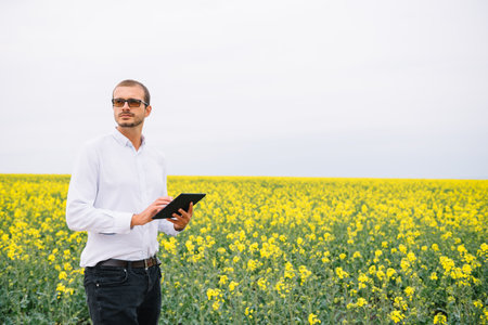 Young agronomist holds tablet in rape field. Agribusiness concept. agricultural engineer standing in...