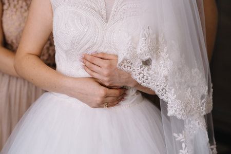 Bridesmaid preparing bride for wedding day. Bridesmaid helping bride fasten lacing her wedding white dress before ceremony. Luxury bridal dress close up. Wedding morning moments details conceptの写真素材
