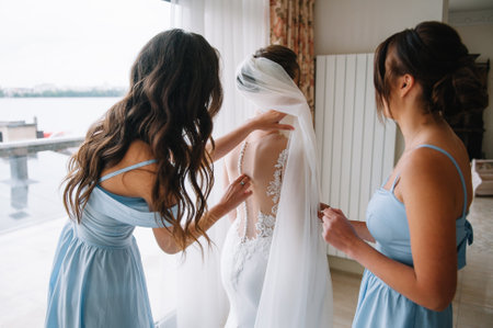 Bridesmaid preparing bride for wedding day. Bridesmaid helping bride fasten lacing her wedding white dress before ceremony. Luxury bridal dress close up. Wedding morning moments details conceptの写真素材