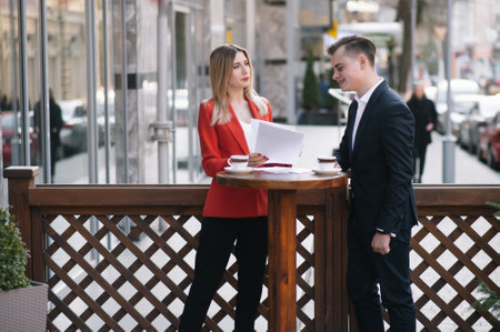 Preparation for meeting. Two young business people standing outside on the city street holding documents looking at each other smiling happy bottom view close-up.の写真素材