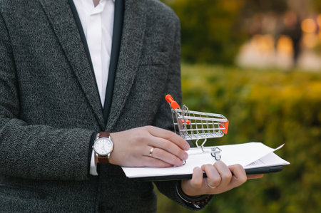 Grocery store chain management, retailing and daily consumer goods trade concept. Business man in a suit with a small miniature shopping cart.の写真素材