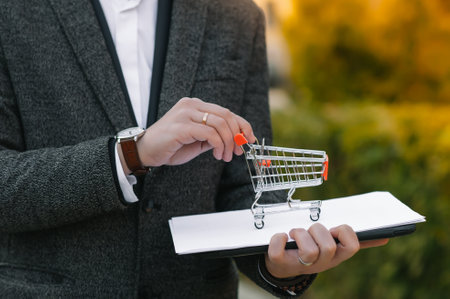 Grocery store chain management, retailing and daily consumer goods trade concept. Business man in a suit with a small miniature shopping cart.の写真素材