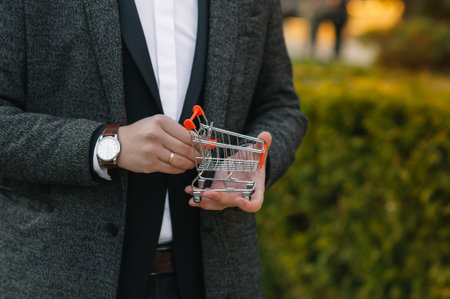 Grocery store chain management, retailing and daily consumer goods trade concept. Business man in a suit with a small miniature shopping cart.の写真素材